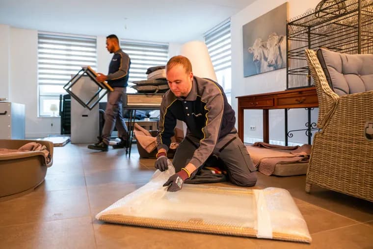 Flyttare skyddar en möbel med plast och filt på golvet
