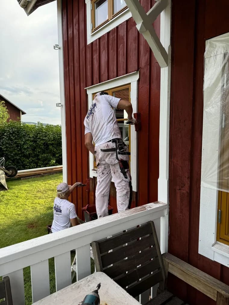 Målare målar en röd träfasad på ett hus