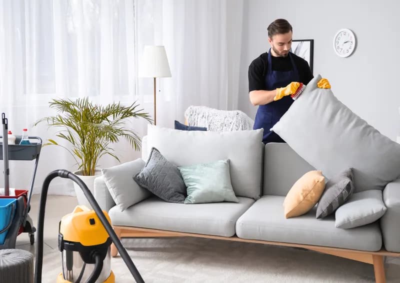 Städare dammsuger och fluffar kuddar i ett ljust vardagsrum